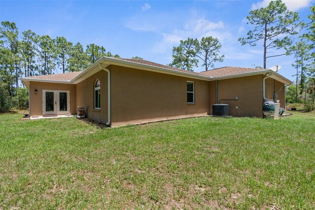 rear view of property with french doors, stucco siding, cooling unit, and a lawn