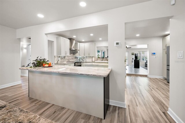 1620 Sea Breeze Dr, Tarpon Springs, FL 34689 - kitchen featuring wall chimney range hood, light wood finished floors, light stone countertops, white cabinetry, and a peninsula