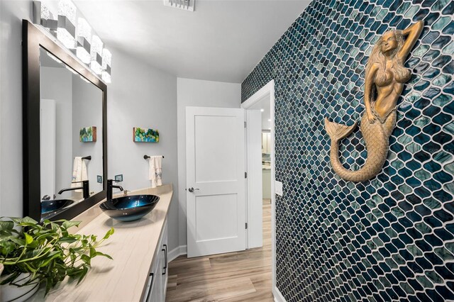1620 Sea Breeze Dr, Tarpon Springs, FL 34689 - bathroom featuring double vanity, an accent wall, wood finished floors, and a tile shower