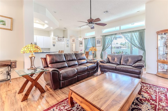 living area featuring ceiling fan, light wood-style flooring, recessed lighting, and a high ceiling