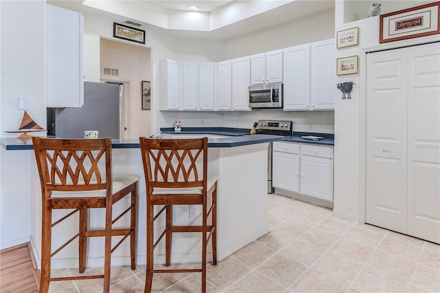 kitchen featuring appliances with stainless steel finishes, a breakfast bar area, a peninsula, dark countertops, and white cabinetry