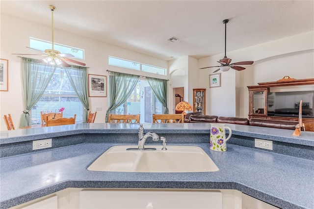 kitchen featuring a ceiling fan, a sink, open floor plan, and dark countertops