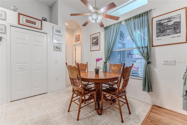 dining area featuring a ceiling fan, arched walkways, light tile patterned floors, and baseboards