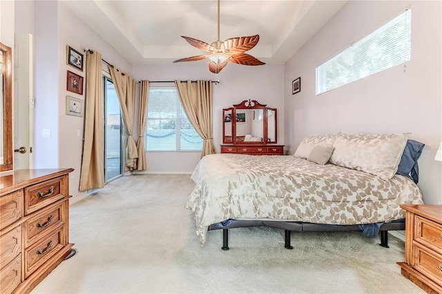 bedroom featuring a tray ceiling, light carpet, access to exterior, and ceiling fan