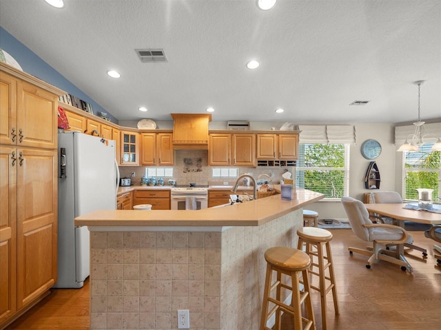 4292 Tahiti Dr, Hernando Beach, FL 34607 - kitchen featuring white appliances, a breakfast bar, light wood finished floors, premium range hood, and a center island with sink