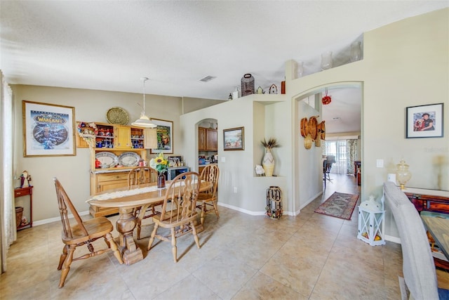 dining area featuring arched walkways, light tile patterned flooring, baseboards, and a textured ceiling