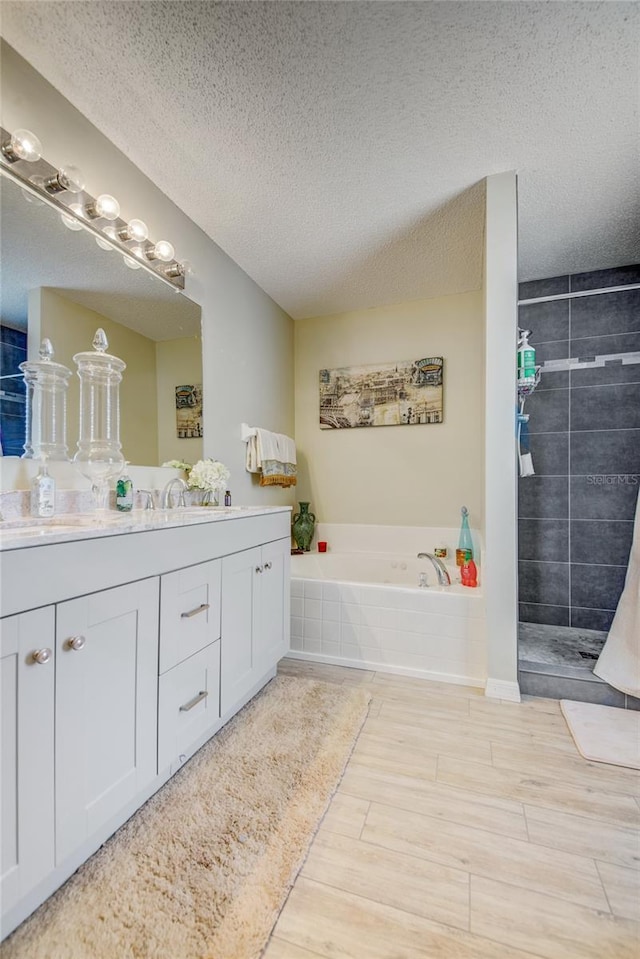 full bath featuring a textured ceiling, a bath, wood finished floors, vanity, and a tile shower