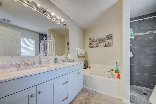 bathroom with tiled shower, a textured ceiling, a tub with jets, wood finished floors, and double vanity