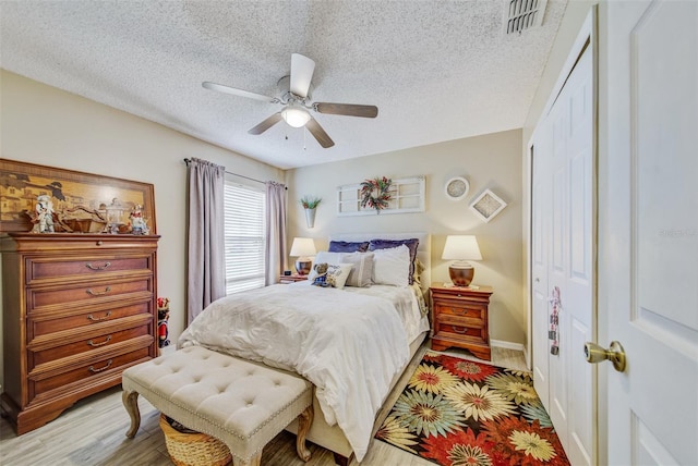 bedroom featuring a closet, a textured ceiling, ceiling fan, light wood-style floors, and baseboards