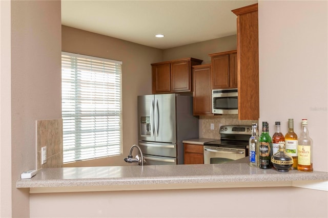 kitchen featuring stainless steel appliances, brown cabinetry, and a peninsula