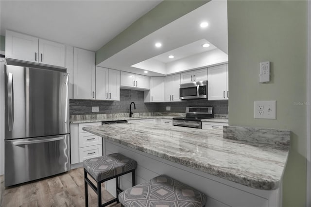 2866 Thistle Ct N, Palm Harbor, FL 34684 - kitchen featuring stainless steel appliances, a kitchen bar, white cabinets, light stone countertops, and a sink