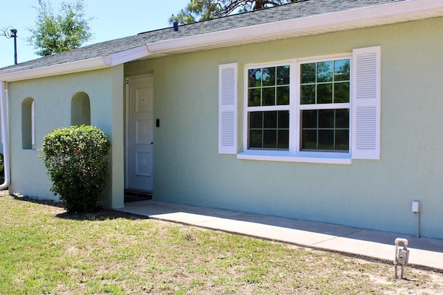 13180 Lawrence St, Spring Hill, FL 34609 - doorway to property featuring a lawn, stucco siding, and a shingled roof