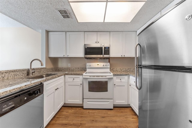kitchen featuring stainless steel appliances, a sink, white cabinetry, light wood-type flooring, and light stone countertops