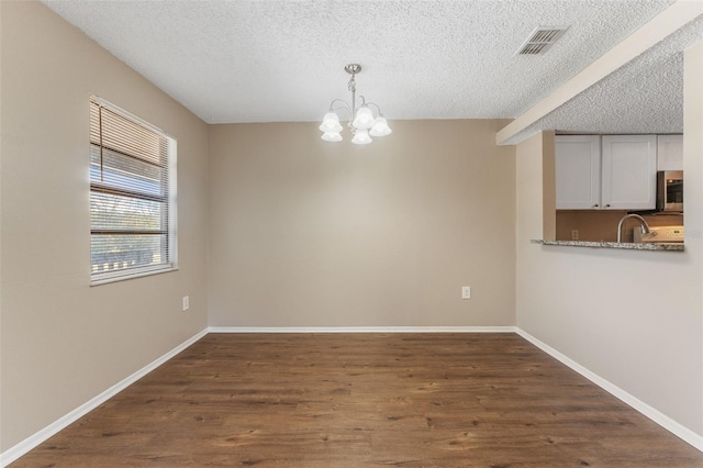 unfurnished dining area with a textured ceiling, a chandelier, dark wood-type flooring, a sink, and baseboards