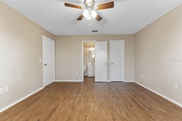 unfurnished bedroom featuring wood finished floors, baseboards, a textured ceiling, ensuite bath, and a ceiling fan