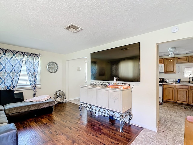 living area with a textured ceiling, baseboards, light wood-style floors, and a ceiling fan