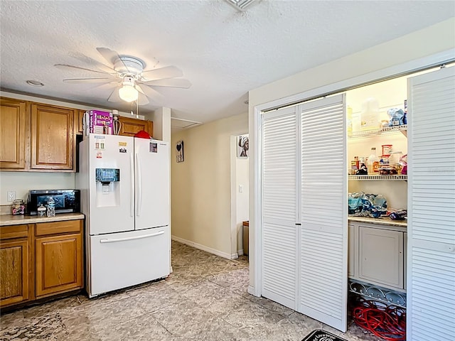 kitchen with white fridge with ice dispenser, brown cabinets, a ceiling fan, light countertops, and a textured ceiling