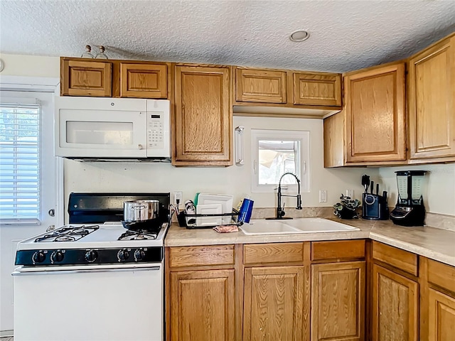 kitchen with white appliances, a sink, a textured ceiling, healthy amount of natural light, and light countertops