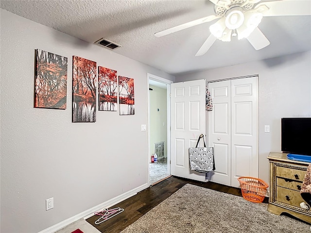 living area with dark wood-type flooring, a ceiling fan, a textured ceiling, and baseboards