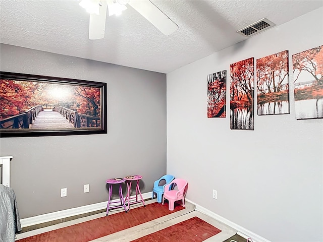 playroom with ceiling fan, a textured ceiling, and baseboards