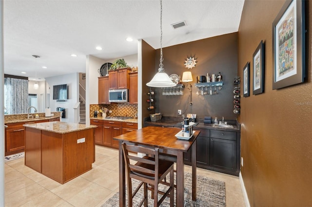 3243 Stonegate Falls Dr, Land O Lakes, FL 34638 - kitchen featuring stainless steel appliances, decorative backsplash, brown cabinets, a center island, and light stone countertops
