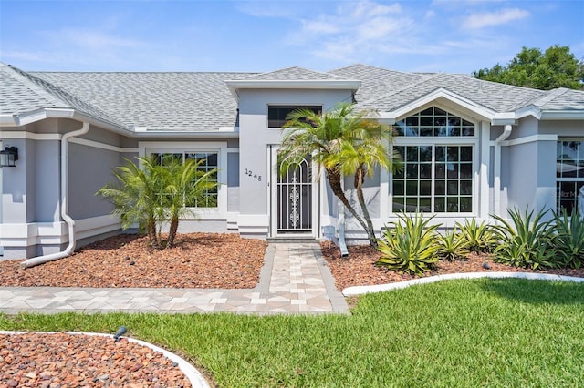 entrance to property with stucco siding and roof with shingles