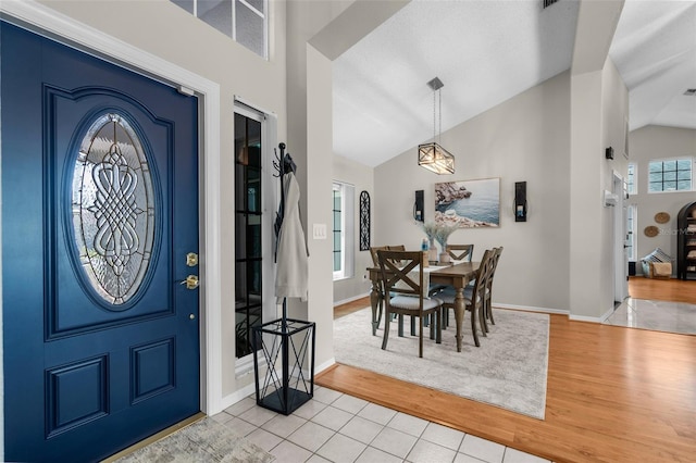entryway featuring light wood finished floors, baseboards, and high vaulted ceiling