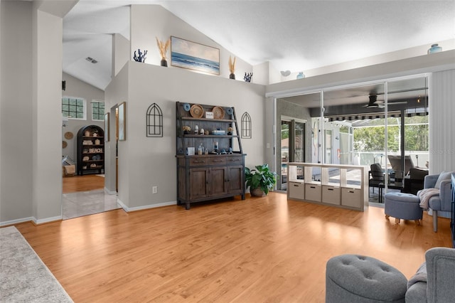 living area featuring ceiling fan, wood finished floors, baseboards, and high vaulted ceiling