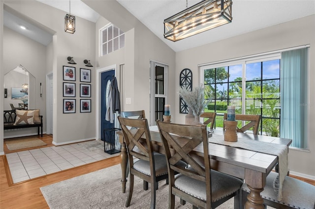 dining area featuring light wood-style flooring, a chandelier, baseboards, and high vaulted ceiling