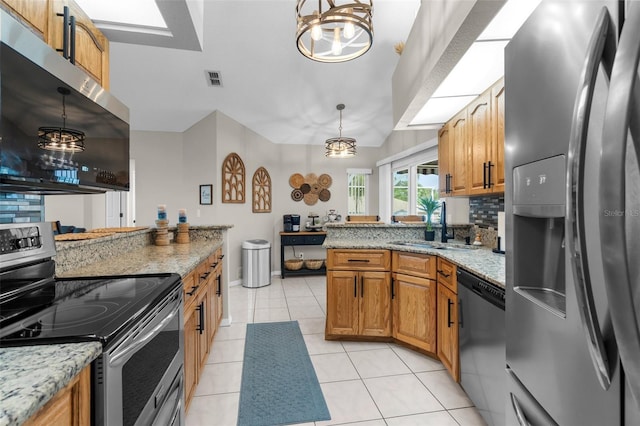 kitchen with stainless steel appliances, a sink, brown cabinetry, light tile patterned floors, and hanging light fixtures