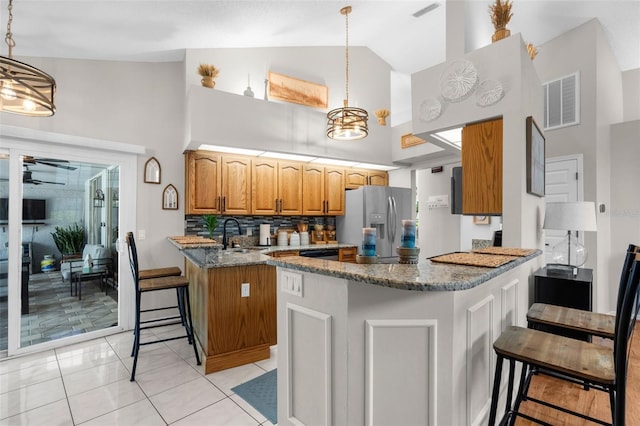 kitchen with stainless steel fridge, a peninsula, high vaulted ceiling, dark stone countertops, and a sink