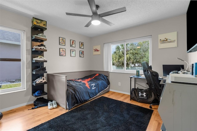 bedroom featuring wood finished floors, a textured ceiling, a desk, a ceiling fan, and baseboards