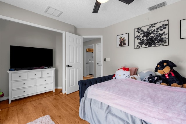 bedroom featuring light wood-type flooring, a textured ceiling, washer / clothes dryer, and a ceiling fan