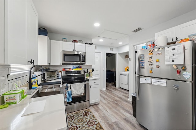 4737 6th St, Zephyrhills, FL 33542 - kitchen with appliances with stainless steel finishes, washer / clothes dryer, white cabinets, backsplash, and light wood finished floors