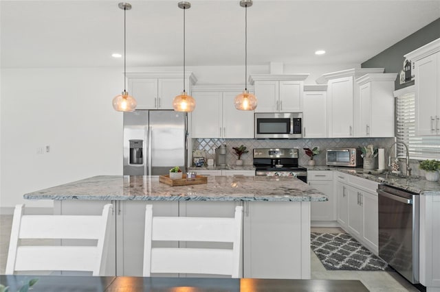 5328 Baldock Ave, Spring Hill, FL 34608 - kitchen featuring appliances with stainless steel finishes, tasteful backsplash, a center island, white cabinetry, and decorative light fixtures