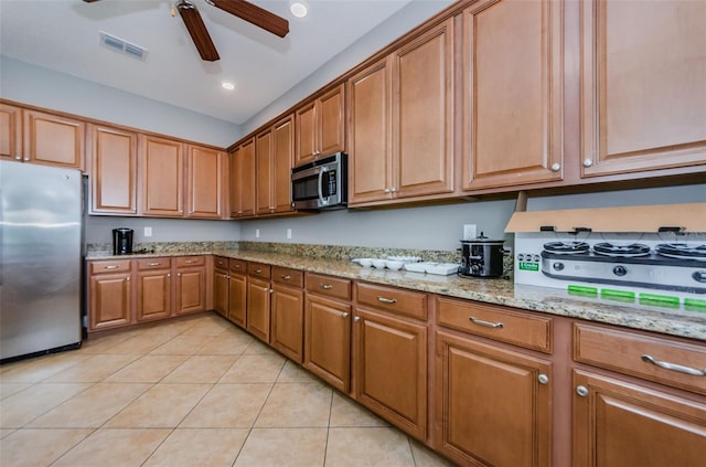 14008 Lugano Ct, Hudson, FL 34669 - kitchen with stainless steel appliances, light tile patterned flooring, brown cabinetry, a ceiling fan, and light stone counters