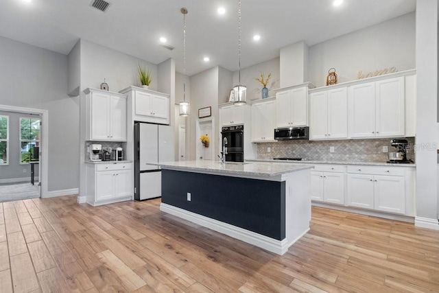 16697 Courtyard Loop, Land O Lakes, FL 34638 - kitchen featuring black appliances, a towering ceiling, white cabinets, backsplash, and a center island with sink