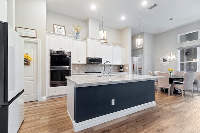 16697 Courtyard Loop, Land O Lakes, FL 34638 - kitchen with black appliances, decorative backsplash, light wood finished floors, white cabinetry, and a towering ceiling