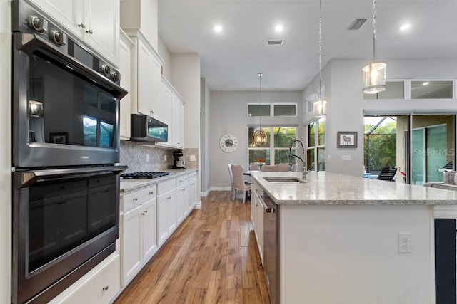 16697 Courtyard Loop, Land O Lakes, FL 34638 - kitchen with appliances with stainless steel finishes, white cabinetry, light wood-style flooring, decorative backsplash, and an island with sink