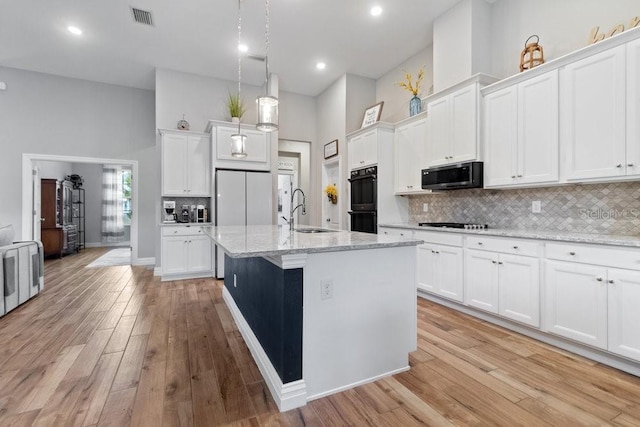 16697 Courtyard Loop, Land O Lakes, FL 34638 - kitchen with stainless steel microwave, a high ceiling, white cabinets, a center island with sink, and light wood-style flooring