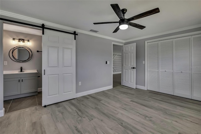 6306 Aberdeen Ave, New Port Richey, FL 34653 - unfurnished bedroom with a barn door, ornamental molding, light wood-type flooring, baseboards, and ensuite bathroom