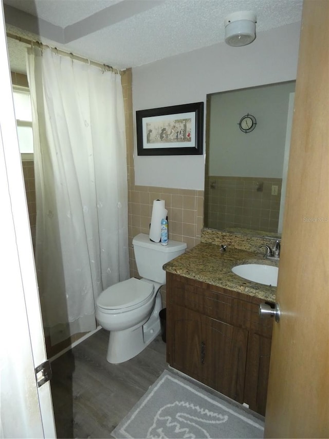 7421 Fairfax Dr, Port Richey, FL 34668 - full bath with wood finished floors, toilet, tile walls, vanity, and a wainscoted wall