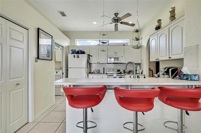 10155 Duffy Cir, Weeki Wachee, FL 34613 - kitchen featuring white appliances, a peninsula, ceiling fan, tasteful backsplash, and a breakfast bar