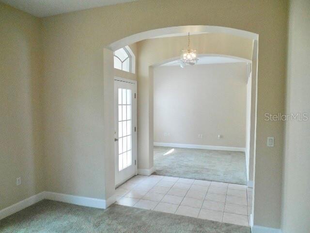 5701 Brackenwood Dr, Spring Hill, FL 34609 - carpeted spare room featuring arched walkways, plenty of natural light, a chandelier, and tile patterned flooring