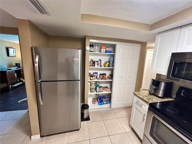 7861 Raintree Dr, New Port Richey, FL 34653 - kitchen featuring stainless steel appliances, white cabinets, light tile patterned floors, light stone countertops, and a textured ceiling