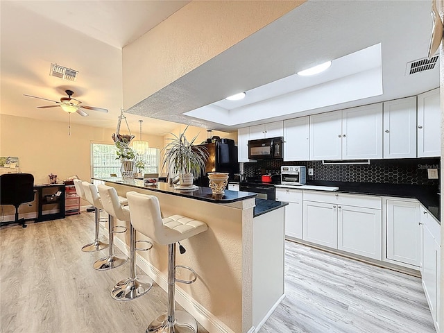 10411 Ireland St, Spring Hill, FL 34608 - kitchen with black appliances, light wood-type flooring, a raised ceiling, and dark countertops