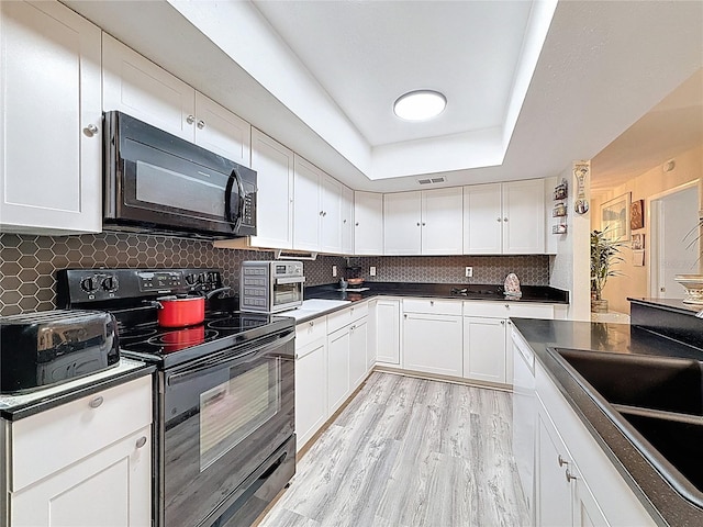 10411 Ireland St, Spring Hill, FL 34608 - kitchen with black appliances, white cabinets, a tray ceiling, backsplash, and dark countertops