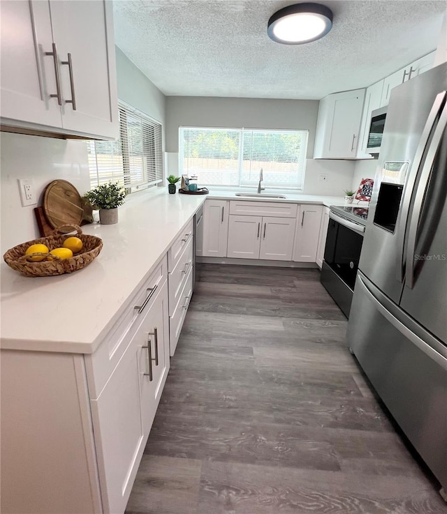 3304 Honeymoon Ln, Holiday, FL 34691 - kitchen featuring stainless steel appliances, a sink, a textured ceiling, dark wood finished floors, and white cabinetry