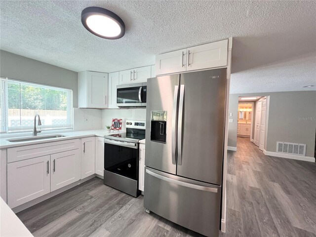 3304 Honeymoon Ln, Holiday, FL 34691 - kitchen with stainless steel appliances, a sink, a textured ceiling, wood finished floors, and white cabinets