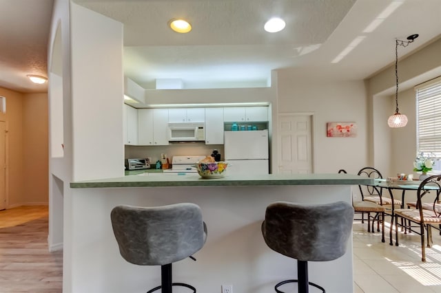 14466 Tamarind Loop, Spring Hill, FL 34609 - kitchen with white appliances, a breakfast bar area, hanging light fixtures, dark countertops, and baseboards